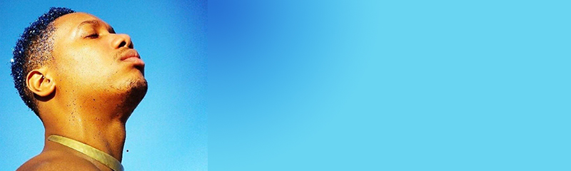feature photo Artist Kalon, has his eyes closed with face facing up towards the sky. He is wearing a gold color necklace, in front of a blue background.